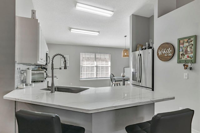 9761 Leeward Way, Navarre, FL 32566 - kitchen featuring stainless steel fridge, a sink, a peninsula, light stone counters, and a breakfast bar area