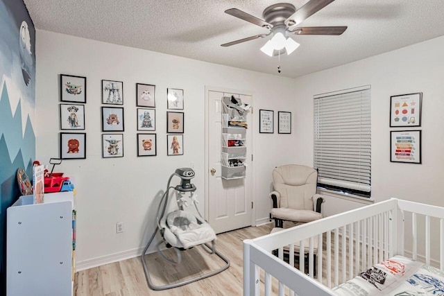 bedroom with ceiling fan, a crib, a textured ceiling, and light hardwood / wood-style flooring