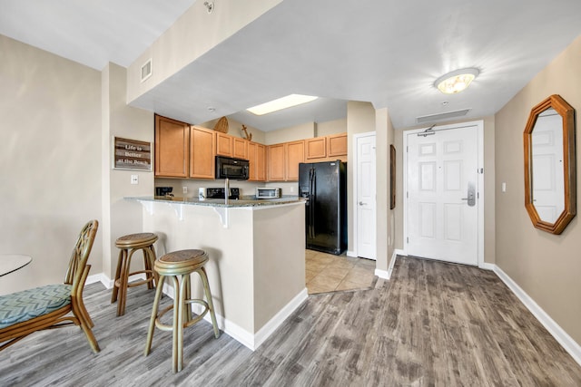 kitchen featuring light stone countertops, light hardwood / wood-style flooring, kitchen peninsula, a breakfast bar, and black appliances