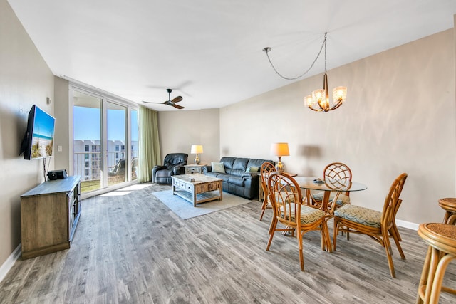 living room featuring ceiling fan with notable chandelier, light hardwood / wood-style floors, and a wall of windows