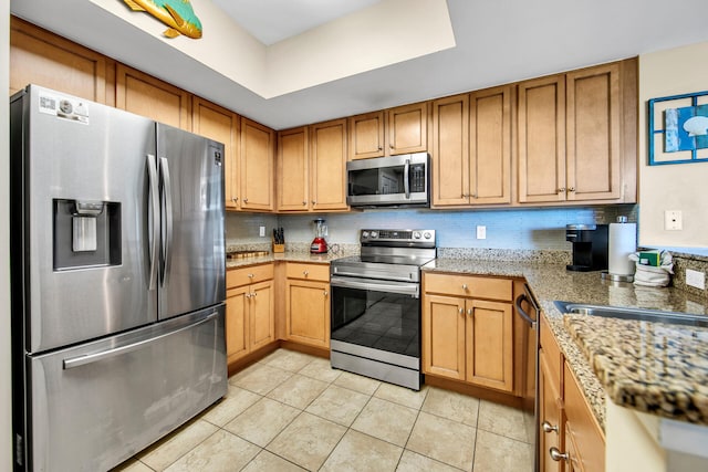 4207 Indian Bayou Trl Unit 2216, Destin, FL 32541 - kitchen with appliances with stainless steel finishes, light tile patterned flooring, brown cabinets, light stone counters, and a tray ceiling