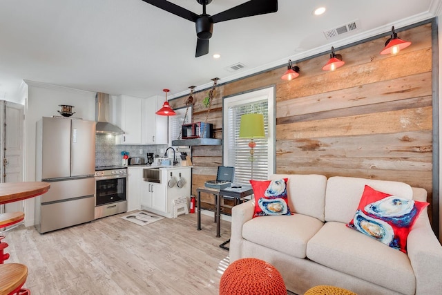 living room featuring ceiling fan, light wood-type flooring, ornamental molding, and wooden walls