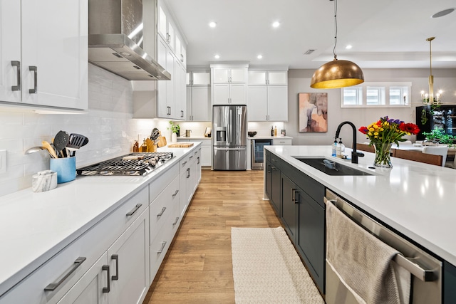 kitchen featuring white cabinets, wall chimney range hood, light wood-type flooring, appliances with stainless steel finishes, and decorative light fixtures