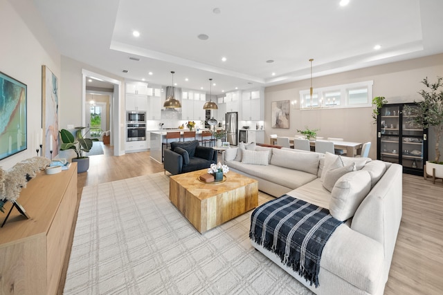 living room featuring a raised ceiling, a notable chandelier, and light wood-type flooring