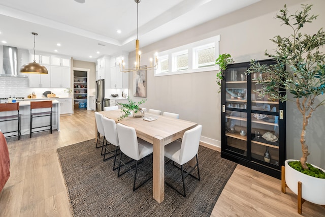 dining space with light hardwood / wood-style floors, an inviting chandelier, and a tray ceiling