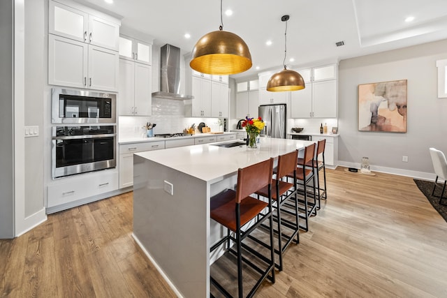 kitchen featuring stainless steel appliances, a center island with sink, white cabinetry, and wall chimney exhaust hood