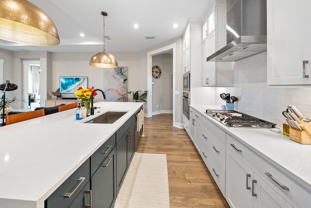 kitchen featuring white cabinetry, sink, wall chimney exhaust hood, and hanging light fixtures