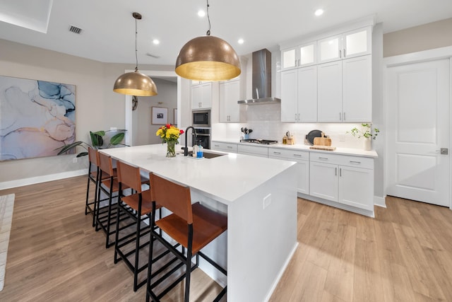 kitchen with wall chimney exhaust hood, white cabinetry, hanging light fixtures, and an island with sink