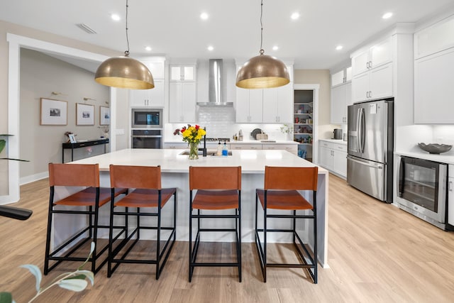 kitchen featuring white cabinets, wall chimney exhaust hood, a spacious island, and stainless steel appliances