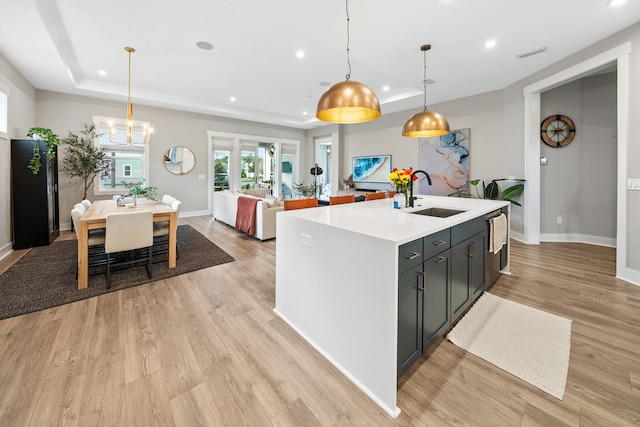 kitchen featuring a kitchen island with sink, a raised ceiling, sink, light hardwood / wood-style flooring, and decorative light fixtures