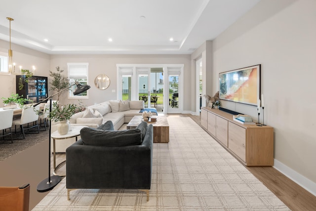 living room featuring an inviting chandelier, light hardwood / wood-style flooring, and a tray ceiling