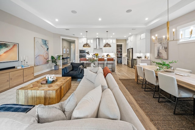 living room featuring a notable chandelier, light wood-type flooring, and a tray ceiling