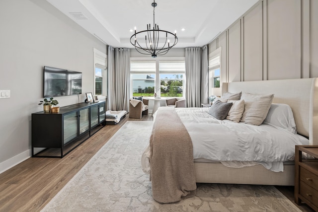 bedroom featuring light hardwood / wood-style floors, a tray ceiling, and an inviting chandelier