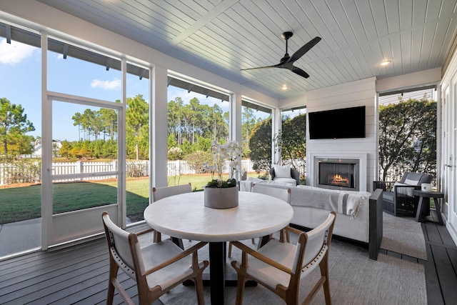 sunroom featuring ceiling fan, a fireplace, and wood ceiling