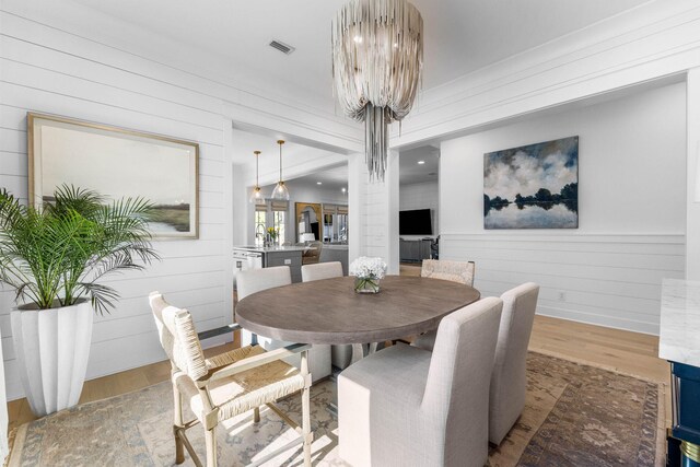 dining room featuring hardwood / wood-style flooring, wooden walls, and a chandelier