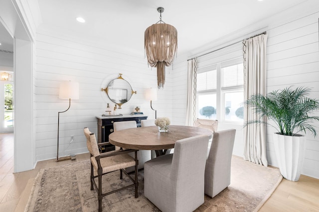 dining area featuring light wood-type flooring, plenty of natural light, ornamental molding, and wood walls