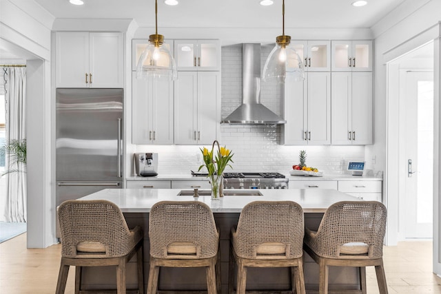 kitchen with light hardwood / wood-style flooring, white cabinets, wall chimney range hood, and appliances with stainless steel finishes