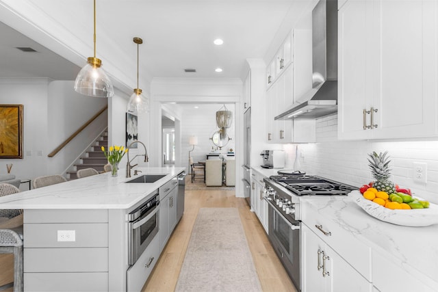 kitchen with sink, hanging light fixtures, wall chimney exhaust hood, white cabinetry, and stainless steel appliances