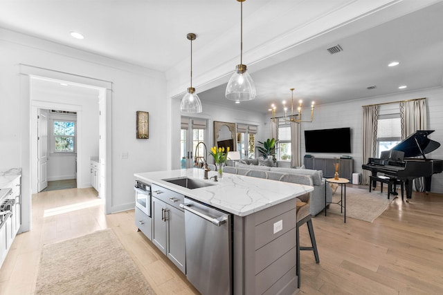 kitchen with appliances with stainless steel finishes, light wood-type flooring, sink, pendant lighting, and an island with sink