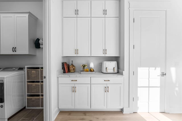 bar with white cabinets, light wood-type flooring, washer / clothes dryer, and light stone counters