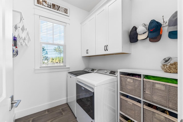 clothes washing area with washing machine and clothes dryer, dark wood-type flooring, and cabinets