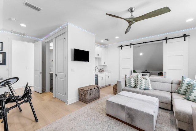 living room featuring ceiling fan, a barn door, and light hardwood / wood-style floors