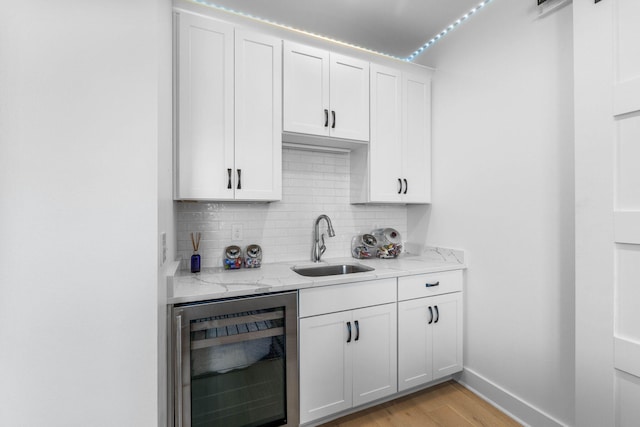 kitchen with wine cooler, white cabinetry, sink, and light wood-type flooring