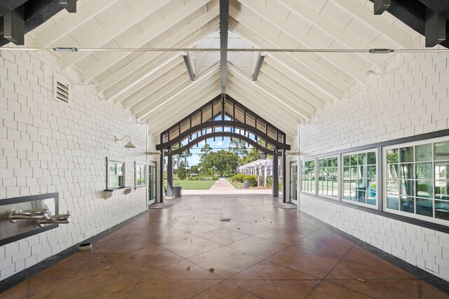 hallway featuring beam ceiling, high vaulted ceiling, and brick wall