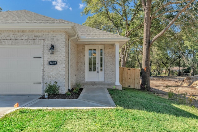 doorway to property featuring a garage, roof with shingles, a lawn, and brick siding