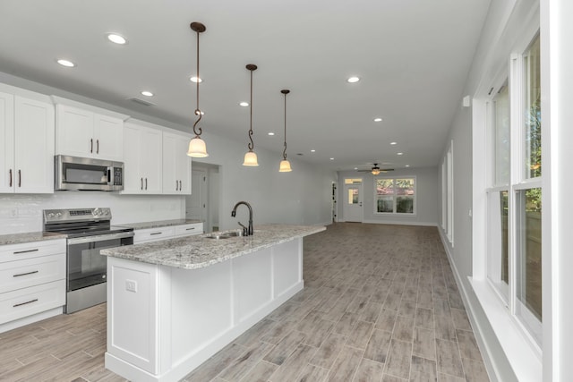 kitchen with white cabinetry, ceiling fan, stainless steel appliances, an island with sink, and decorative light fixtures