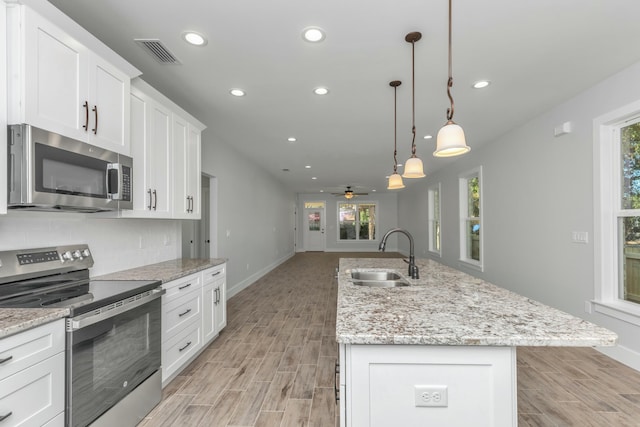 kitchen with stainless steel appliances, ceiling fan, sink, a center island with sink, and hanging light fixtures