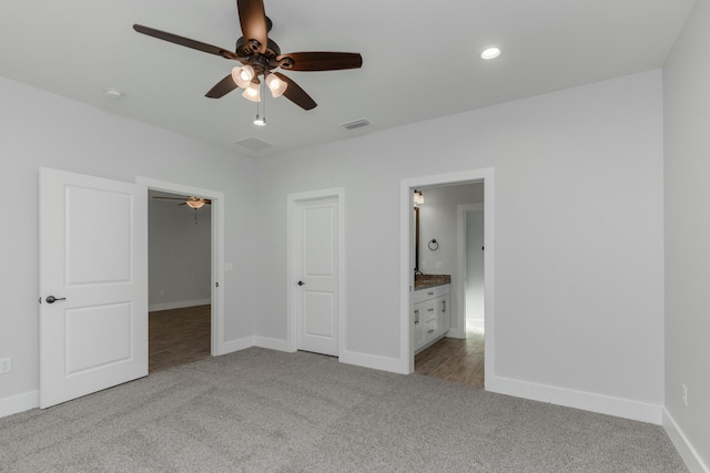 unfurnished bedroom with a closet, connected bathroom, light colored carpet, and ceiling fan