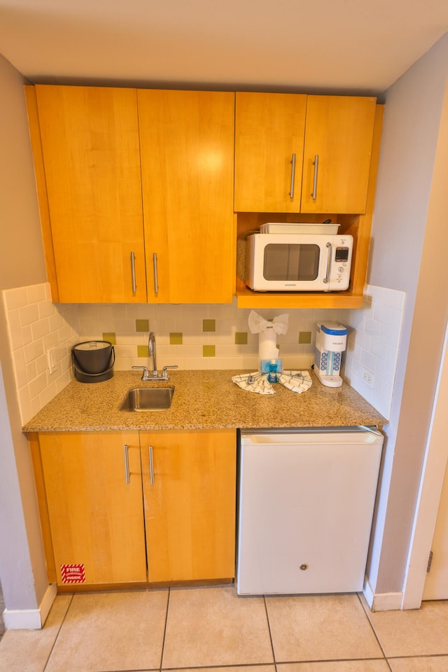 kitchen with light stone countertops, sink, backsplash, white appliances, and light tile patterned floors