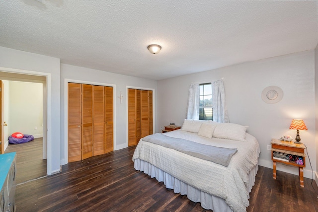 bedroom featuring a textured ceiling, multiple closets, and dark wood-type flooring