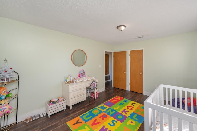 bedroom with dark hardwood / wood-style flooring, a crib, and a textured ceiling