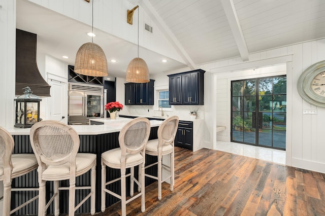 kitchen with custom exhaust hood, sink, stainless steel built in fridge, vaulted ceiling with beams, and dark hardwood / wood-style floors