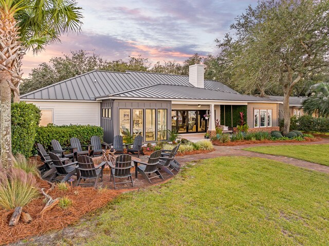 back house at dusk featuring a fire pit, a patio, and a lawn