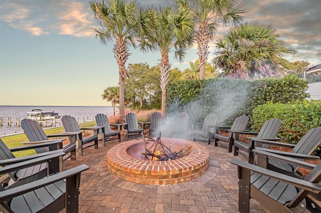 patio terrace at dusk featuring a water view and a fire pit