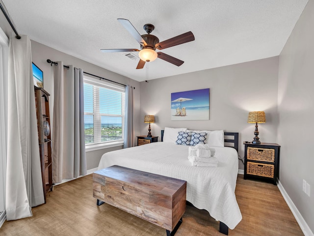 bedroom with ceiling fan, a textured ceiling, and light hardwood / wood-style floors