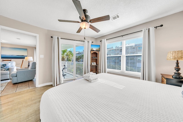 bedroom with multiple windows, access to exterior, light hardwood / wood-style floors, and a textured ceiling