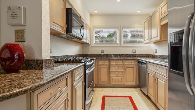 kitchen with appliances with stainless steel finishes, light tile patterned floors, and dark stone countertops