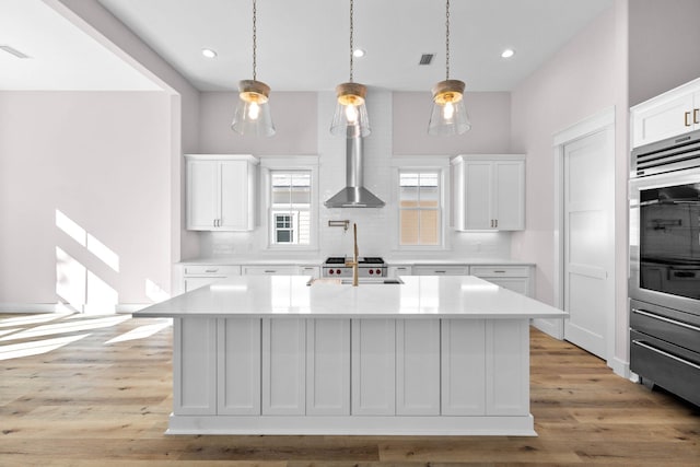 kitchen with white cabinetry, an island with sink, and light wood-type flooring