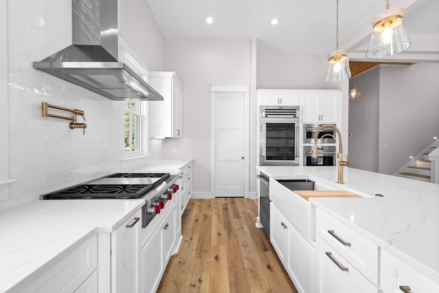 kitchen featuring wall chimney exhaust hood, white cabinetry, light wood-type flooring, and hanging light fixtures