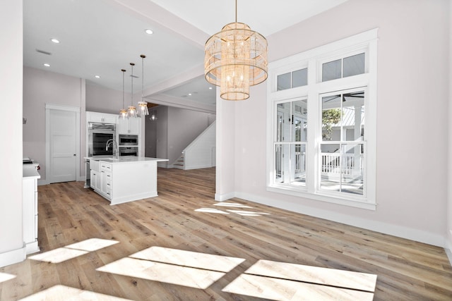 kitchen with pendant lighting, a center island with sink, light wood-type flooring, and white cabinets