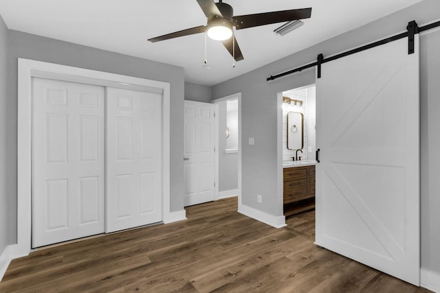 unfurnished bedroom with a barn door, dark hardwood / wood-style floors, ceiling fan, and connected bathroom