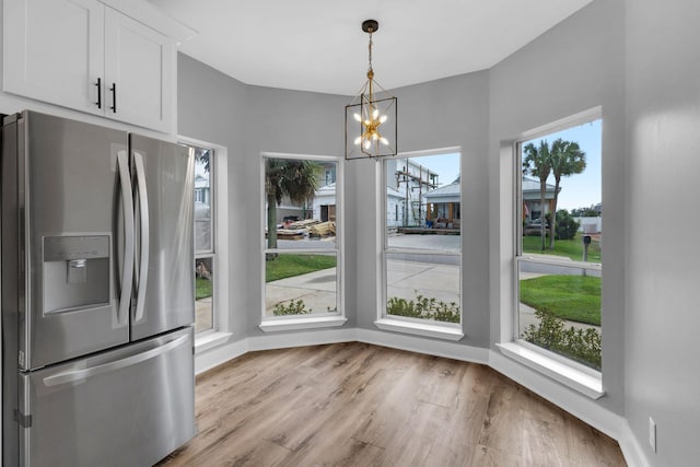 unfurnished dining area with a notable chandelier, a wealth of natural light, and light hardwood / wood-style flooring