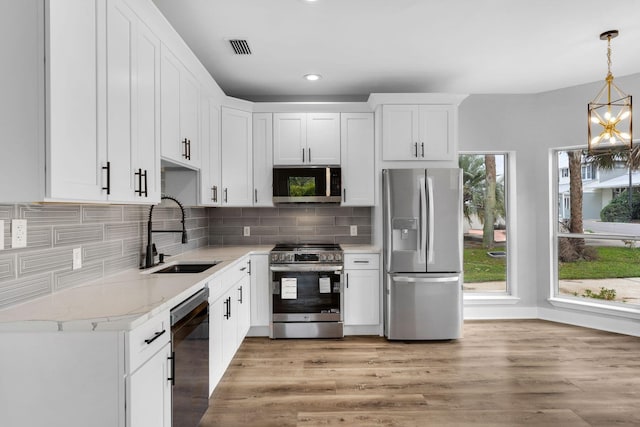 kitchen featuring stainless steel appliances, sink, light hardwood / wood-style flooring, white cabinetry, and hanging light fixtures