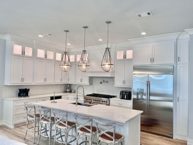 kitchen featuring white cabinetry, high quality appliances, a kitchen island with sink, and decorative light fixtures