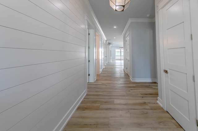 corridor with light wood-type flooring and crown molding