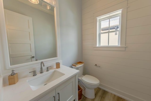 bathroom featuring wooden walls, vanity, wood-type flooring, and toilet